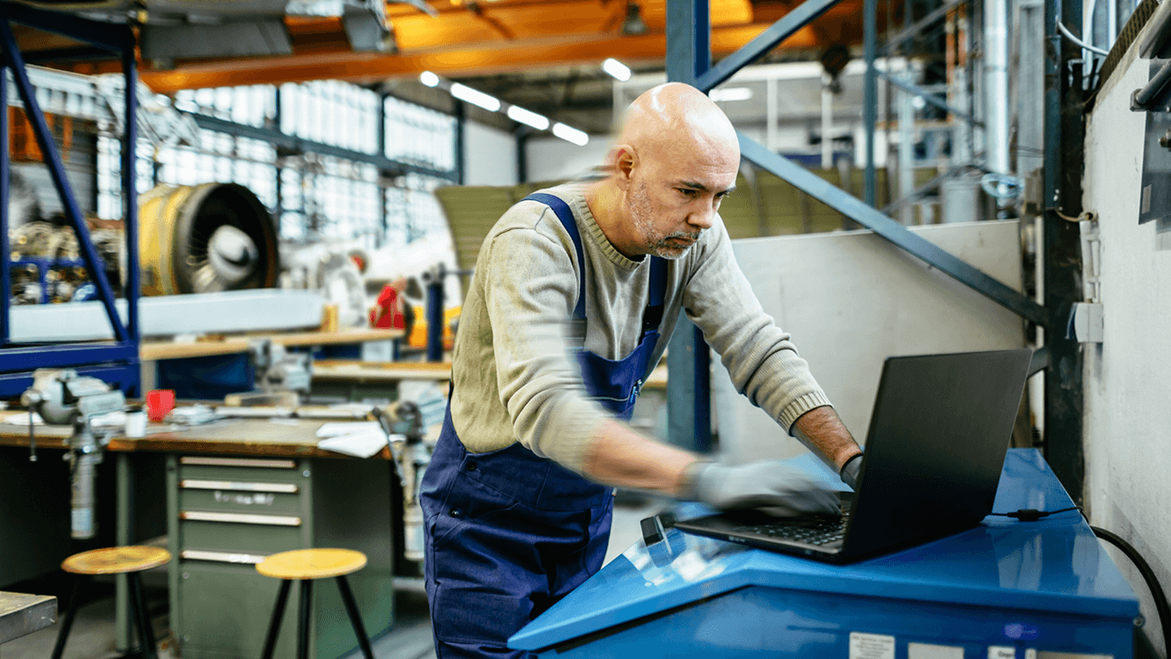 man in overalls in a factory, working on a laptop