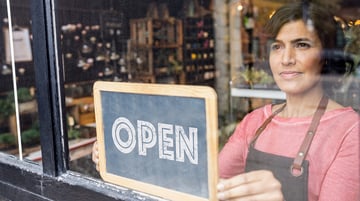 woman opening her shop, flipping a sign to Open