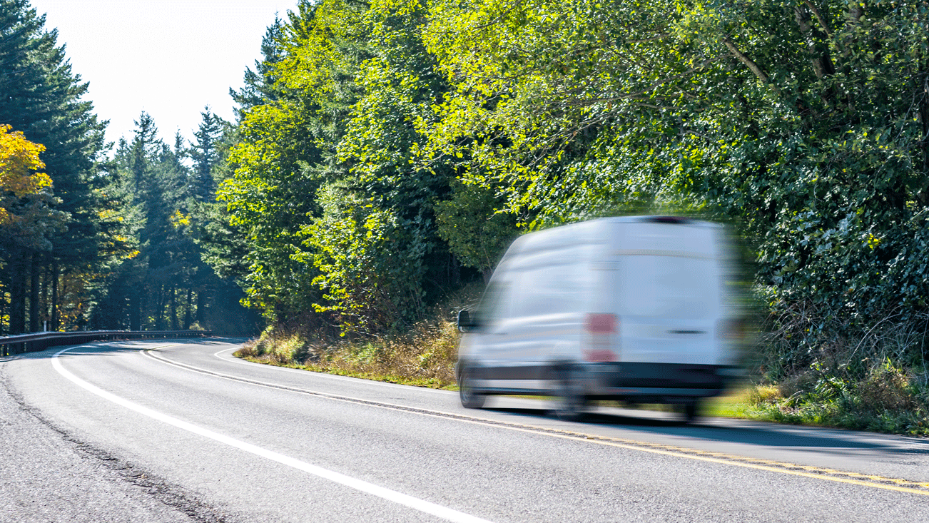 White cargo van on a road next to a forest