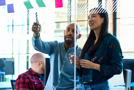 Black man and asian woman planning with sticky notes on a glass wall