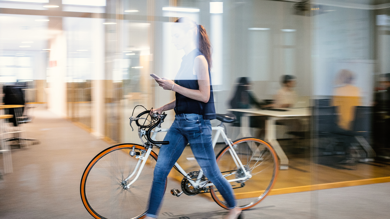 women in jean walking in an office with her bike