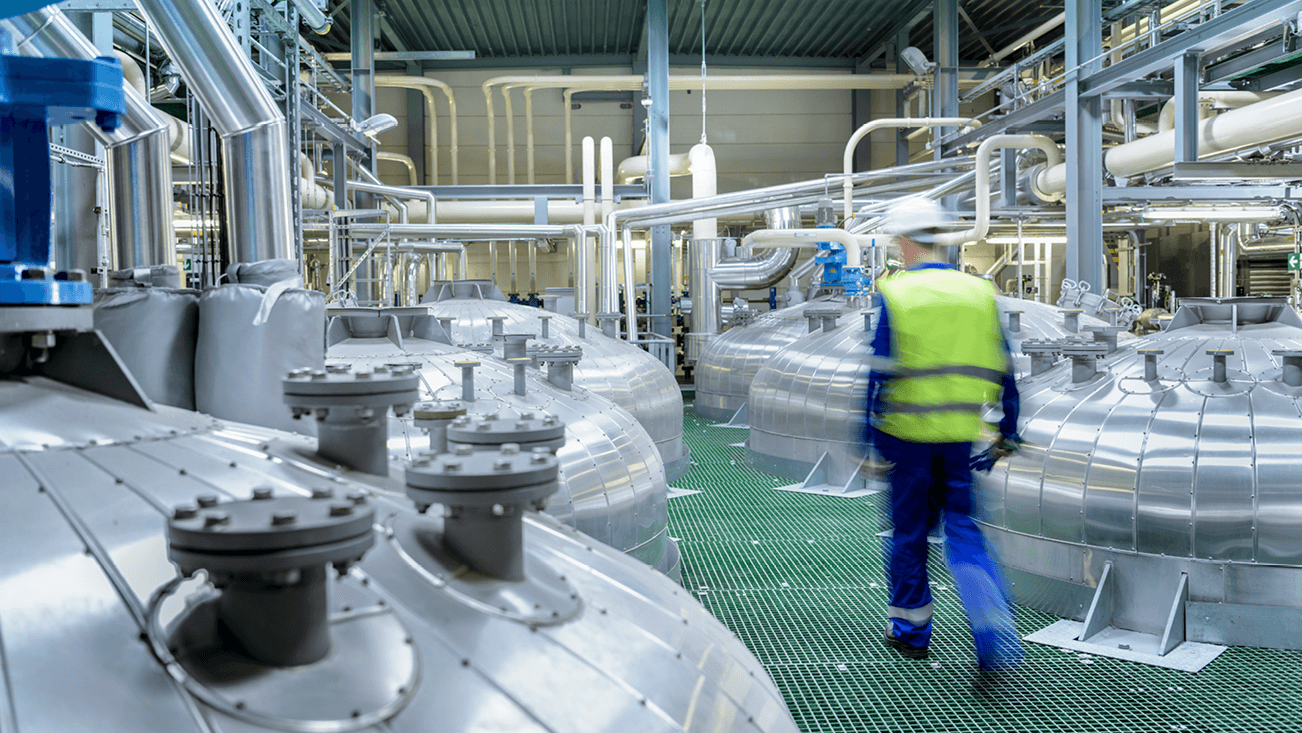 man with yellow jacket and white helmet, walking in a factory