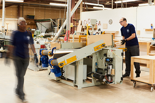 White man cutting wood plank while black woman pass by in a wood workshop