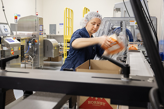White woman employee unpacking box and putting it on a carousel in a food factory