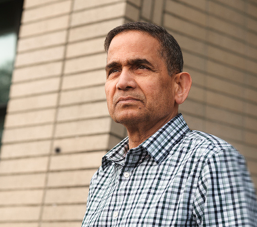asian men looking away with blue shirt next to brick wall