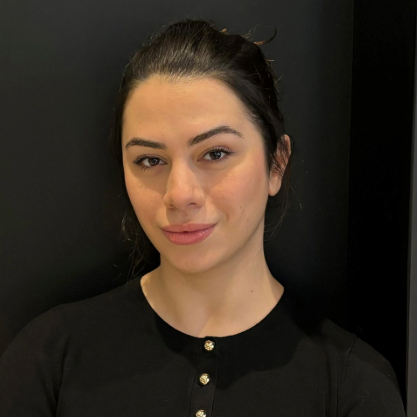 Women wearing a black top is standing against a dark background.