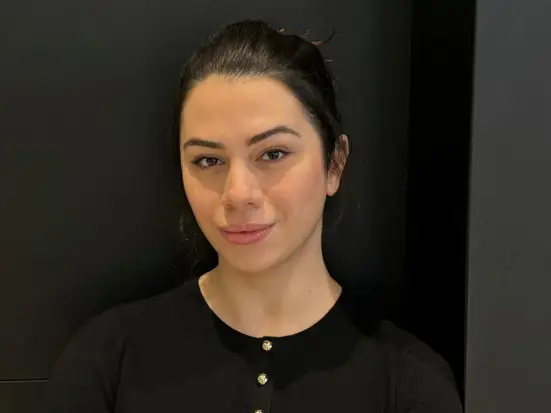 Femme portant un haut noir, se tient contre un fond sombre