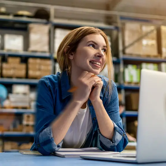 young woman working in a warehouse on a laptop
